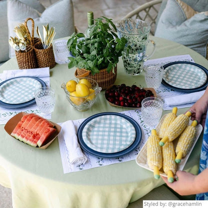Table setting with white floral paper placemats layered with blue and blue ginham dishes with fresh fruit and vegetables