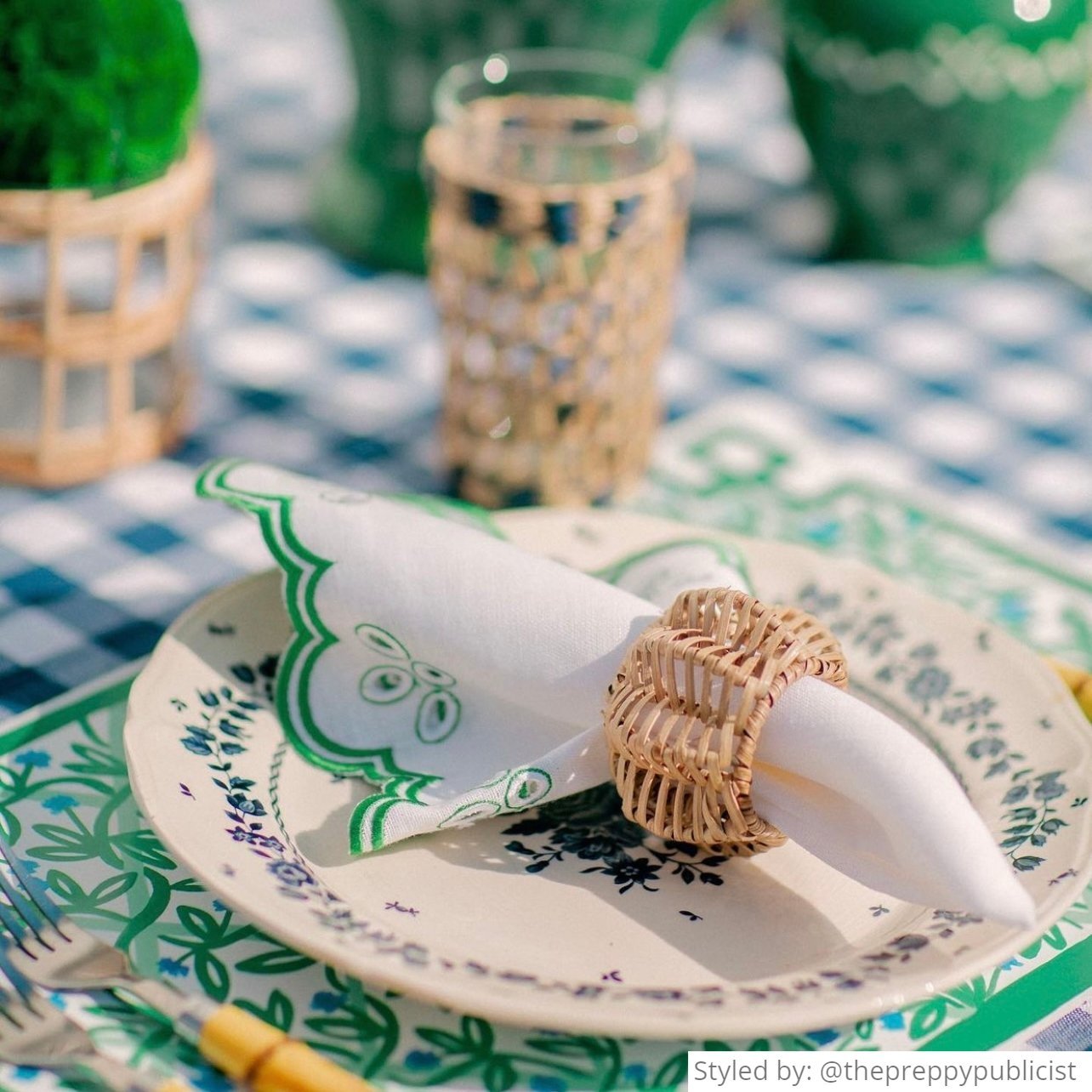 Outdoor place setting with a green and white paper placemat layered with a green and blue dish and a green and white napkin with a rattan napkin ring