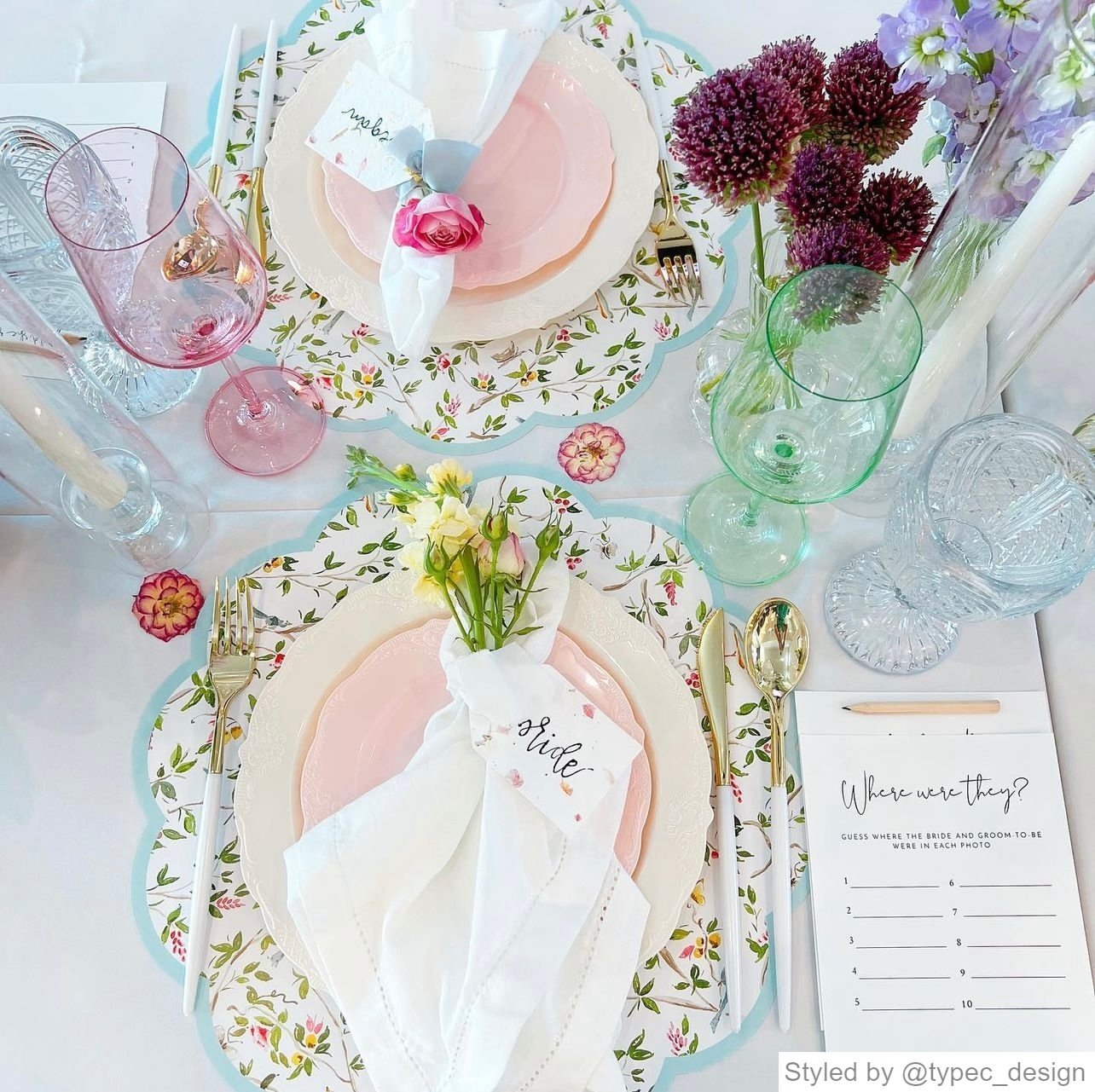 Table setting with chinoiserie round scalloped paper placemats layered with white and pink plates and other pink, blue and green table decor