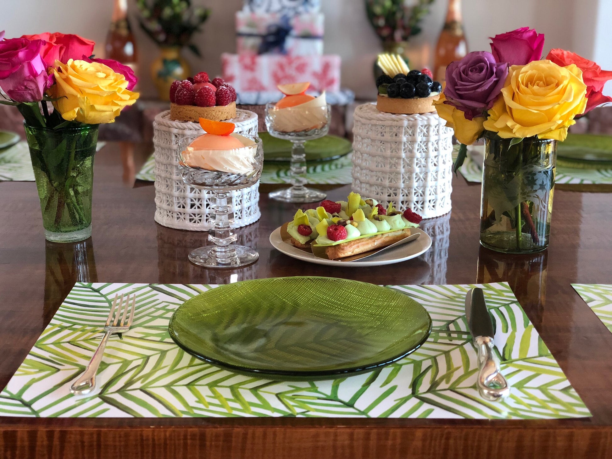 Green leaf paper placemat on table with two vases of colorful roses