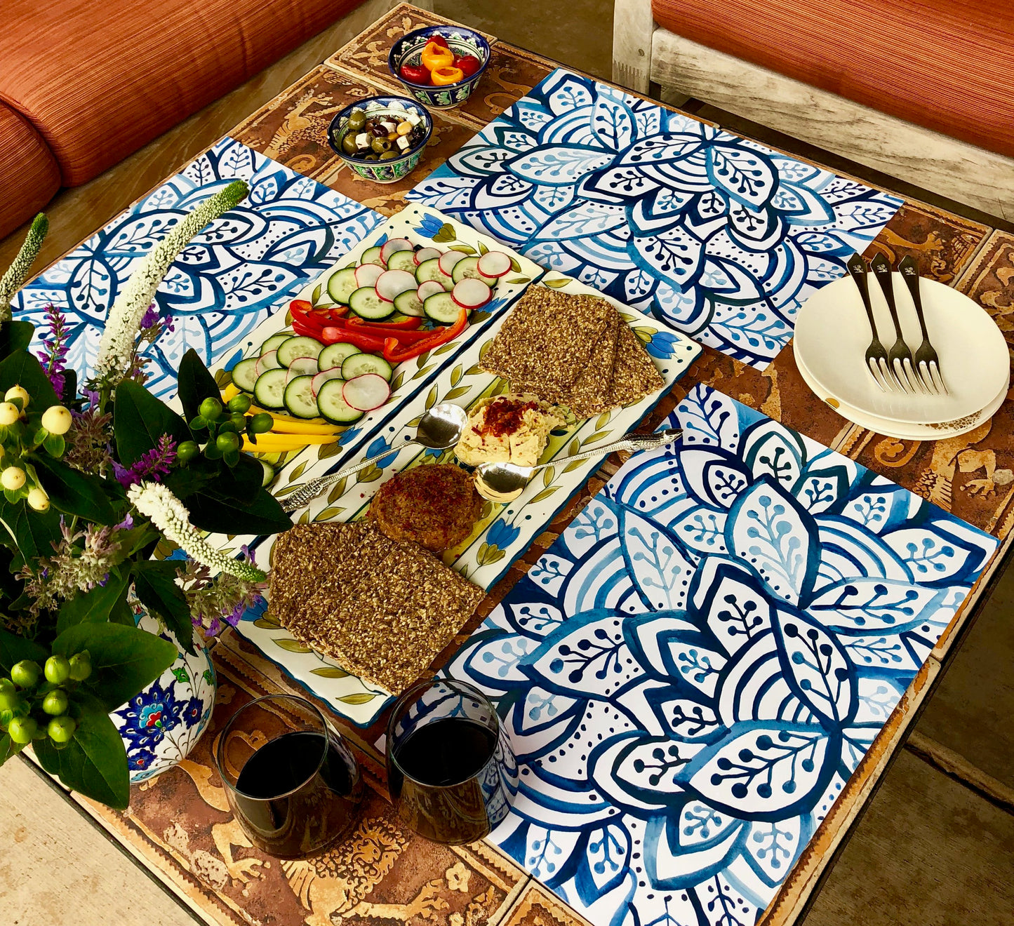 Table setting with blue and white paper placemats, two glasses of wine and some appetizers