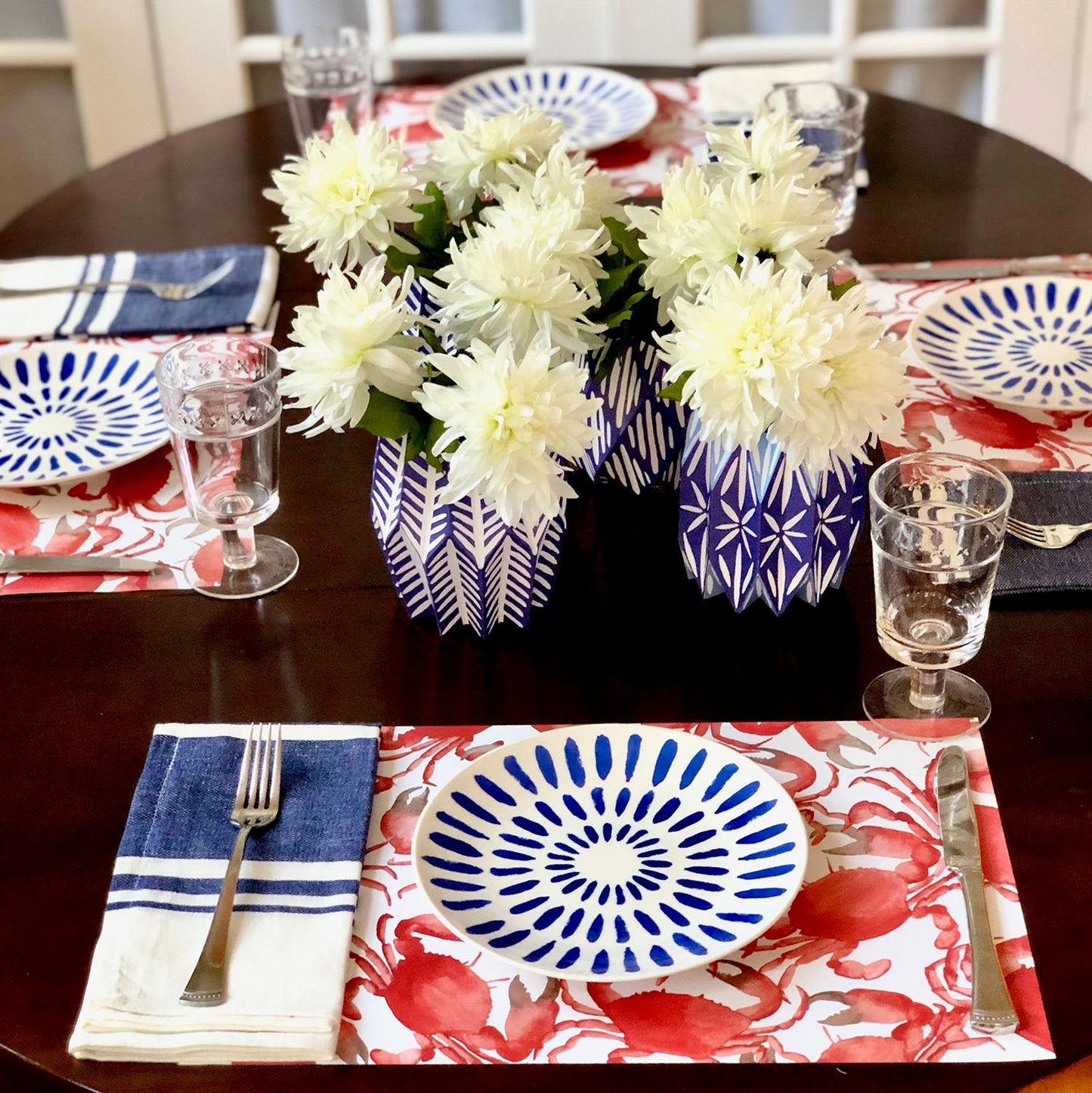 Table setting with red and white crab paper placemats layered with blue and white plates and blue and white vases with white flowers