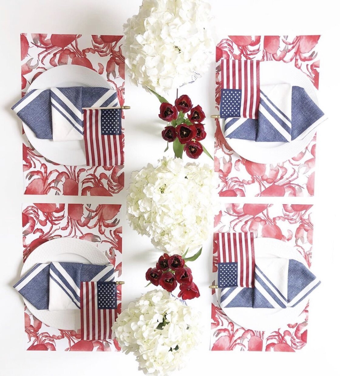 Four place settings on a white table with crab paper placemats, mini American flags and red and white flowers