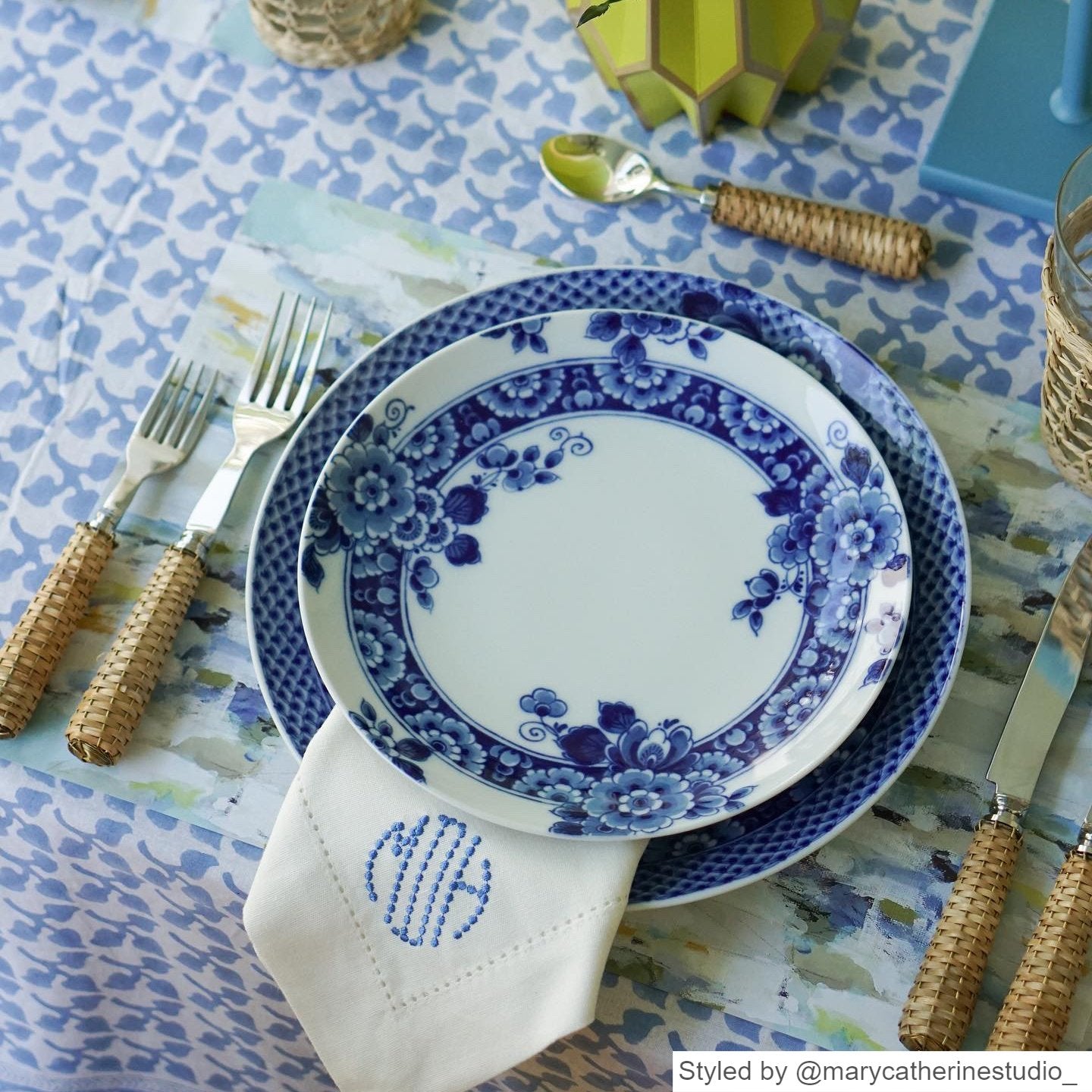 Blue and gray watercolor paper placemat layered with blue and white plates on a blue and white tablecloth