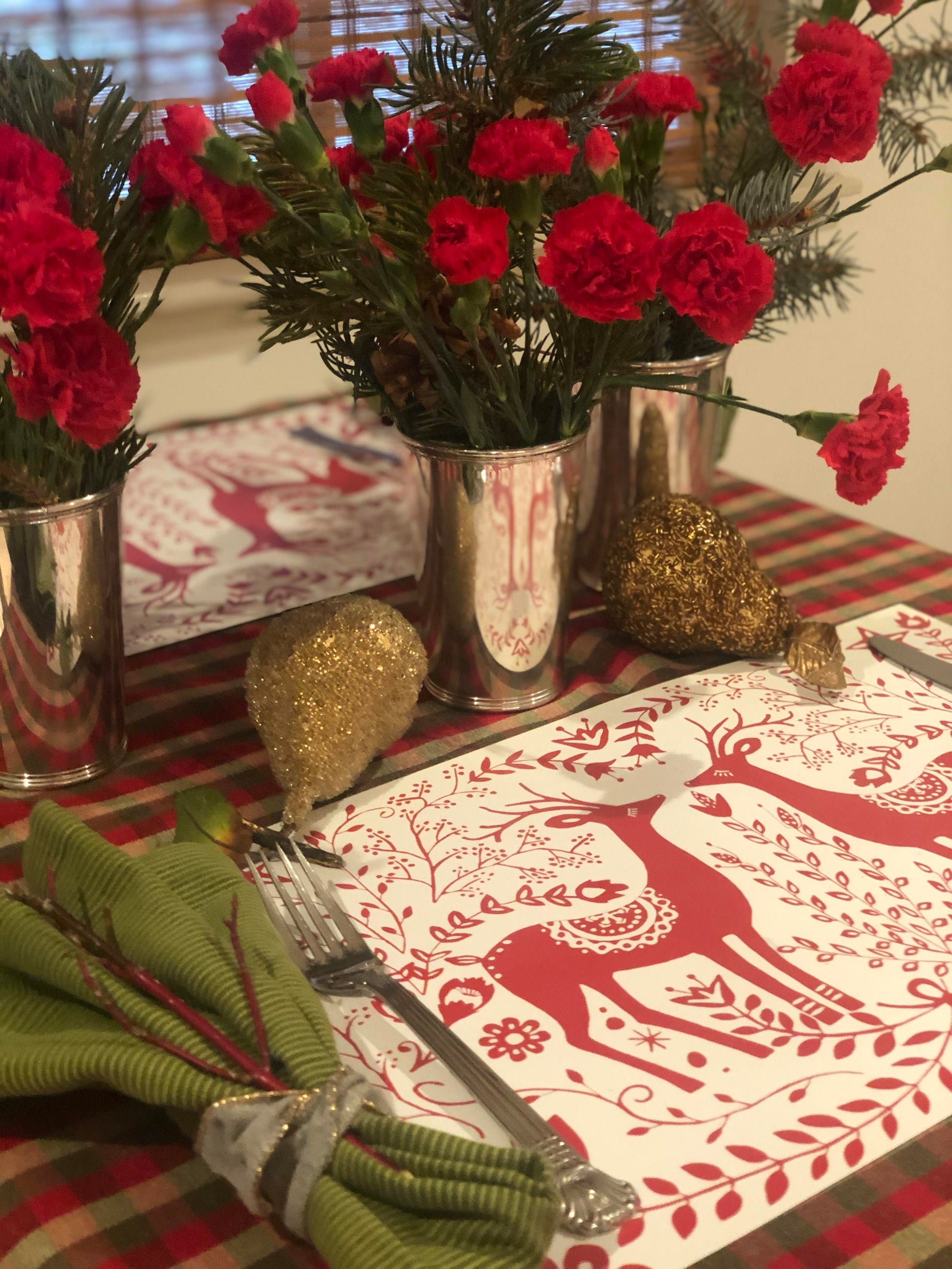 Christmas place setting with red and whiteReindeer Paper Placemats and red flowers.