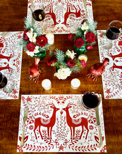 Christmas table setting with red and white Reindeer Paper Placemats and red and green flowers.