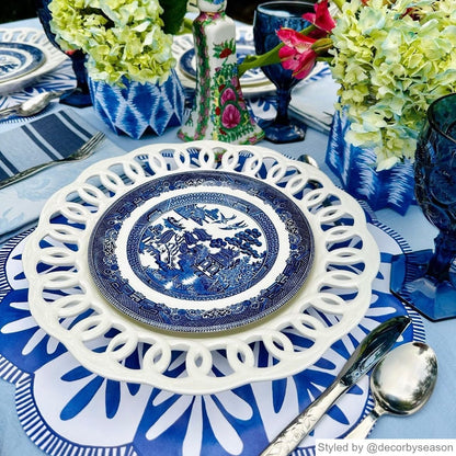 Table setting with blue and white round scalloped paper placemat layered with blue and white dishes and other blue and white table decor
