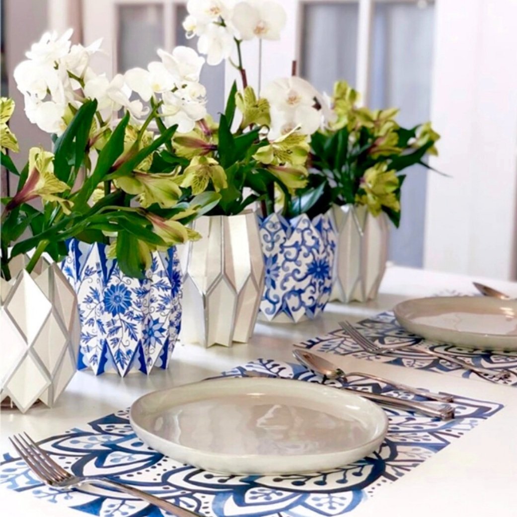 Table setting with a blue and white paper placemat and alternating white and blue paper vases with flowers
