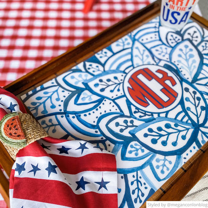 Personalized paper placemat in a tray featuring a blue and white leaf pattern and a red monogram