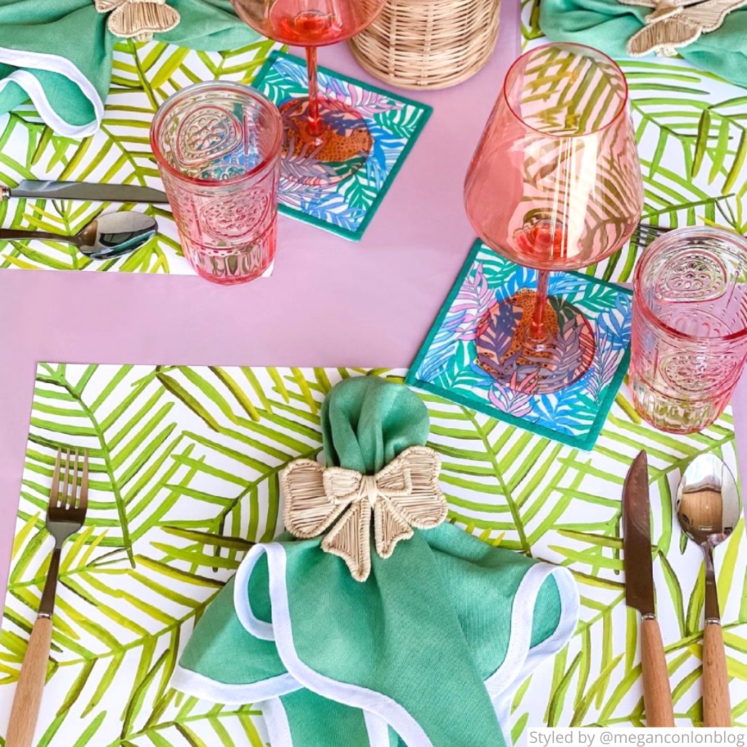 Green leaf paper placemat with green cloth napkins, pink wine glasses, and floral cocktail napkins