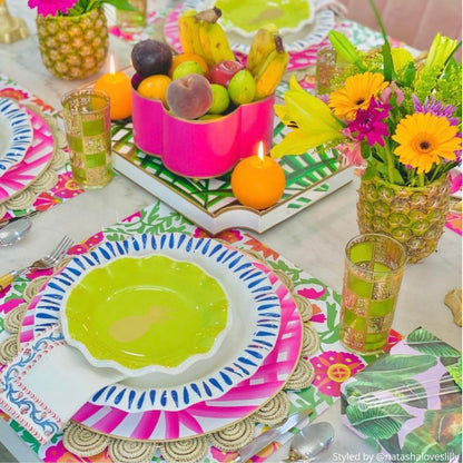 Brightly colored table setting with pink, orange and green floral paper placemats layered with pink and blue plates and pineapple vases