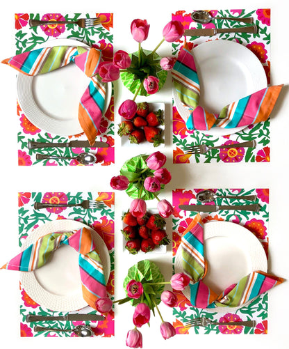 Table setting with pink, orange and green floral paper placemats and colorful napkins and flowers
